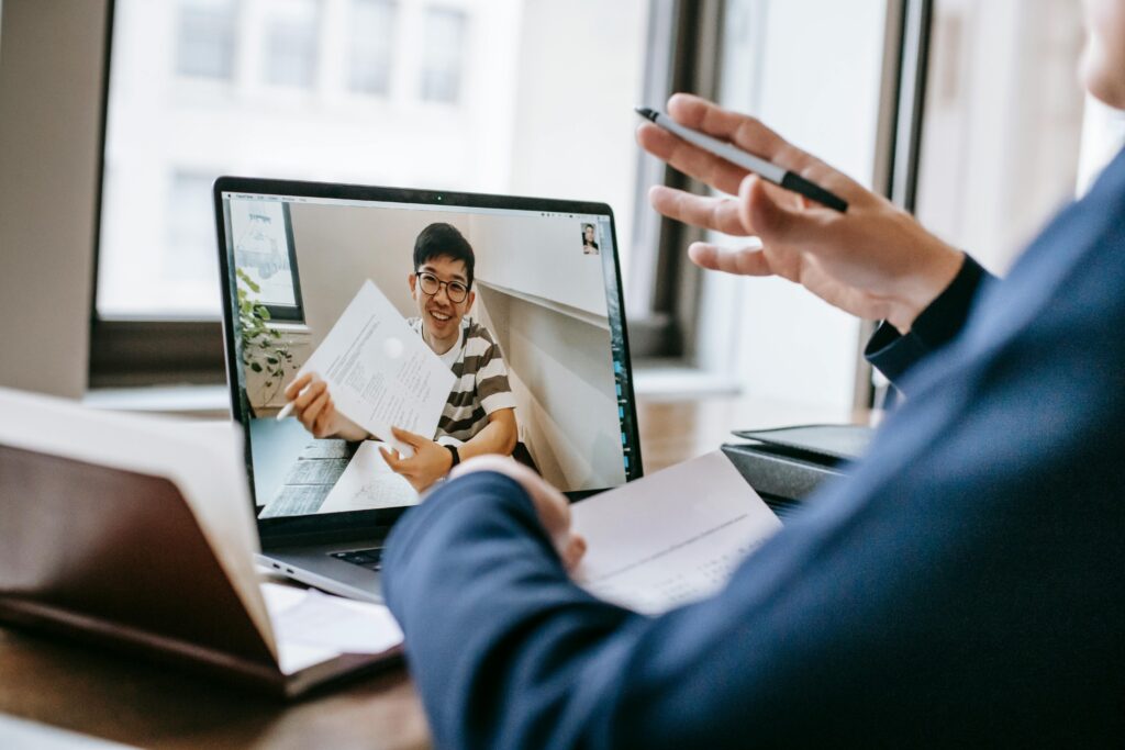 student holding up paper on laptop screen for teacher to see