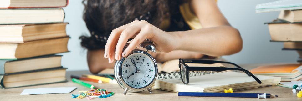 woman with cluttered desk and hand resting on alarm clock