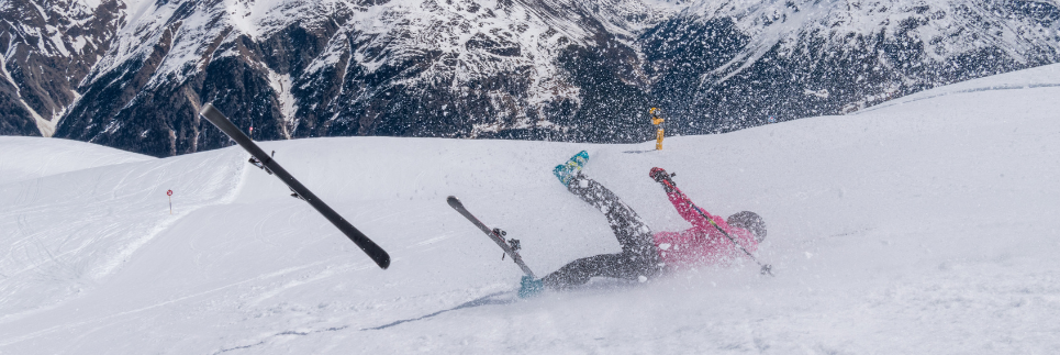 a skiier falling on a snowy hill and a ski going flying